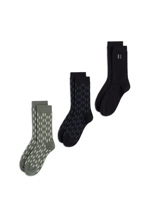 Drei Paar knielange Socken im olivgrün-weißen Muster, marineblau-schwarzen Muster und einfarbig schwarz mit kleinem Logo nahe dem oberen Rand.