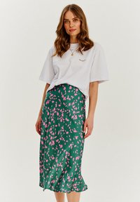 Biała koszulka z małym, wielokolorowym haftowanym wzorem, w połączeniu z zieloną spódnicą midi z różowym abstrakcyjnym wzorem liści.