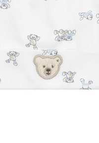 Witte stof met een patroon van kleine teddyberen in blauwe en beige tinten. Bevat een geborduurd berenhoofd in een lichte kleur in het midden.