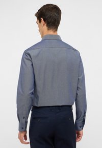 Camicia a maniche lunghe, con bottoni, in un tessuto blu testurizzato. Presenta un colletto classico e polsini con bottone, che si estende in una vestibilità liscia e su misura.