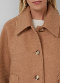 Cappotto di lana marrone con colletto, due tasche frontali e grandi chiusure a bottone. Tessuto testurizzato con una finitura morbida.