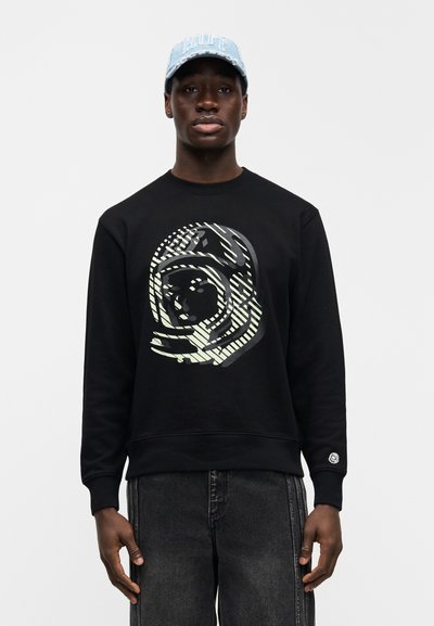 Μαύρο φούτερ με μεγάλο γραφικό σχέδιο σε ανοιχτό πράσινο και γκρι αποχρώσεις. Συνοδεύεται από ανοιχτό μπλε καπέλο με κείμενο στο μπροστινό μέρος.