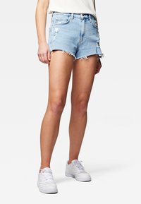 Vaaleansiniset farkkushortsit, joissa on kulutettu muotoilu, repaleinen helma ja taskut. Yhdistetty valkoisiin tennareihin rentoa ilmettä varten.