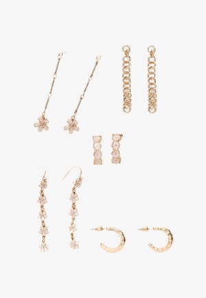 Fem par øreringe i gylden tone med blomsterdesigns, kæder og hoops, vist på en hvid baggrund, der fremviser forskellige længder og stilarter.