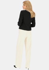 Czarna tweedowa marynarka o strukturalnym kroju, z białym kołnierzykiem i postrzępionym dołem, zestawiona z kremowymi spodniami o szerokich nogawkach i czarnymi szpilkami.