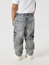 Pantalones de mezclilla gris con un corte relajado, cinturilla elástica y múltiples bolsillos traseros. Sin patrones visibles; textura de superficie lisa.