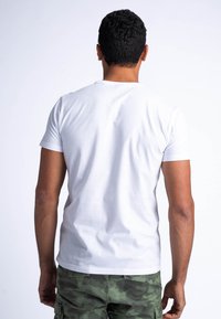 Camiseta de algodón blanca con cuello redondo y mangas cortas, combinada con pantalones cortos de camuflaje verde oliva. La vista trasera muestra un diseño y un ajuste simples.
