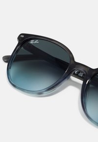 Ochelari de soare Ray-Ban cu un gradient negru și rame supradimensionate. Design din plastic semi-transparent, lentile întunecate și logo în colțul din stânga sus.