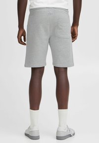 Shorts en coton gris avec une taille à cordon, poche latérale et une coupe décontractée, associés à des chaussettes blanches et des chaussures gris clair.