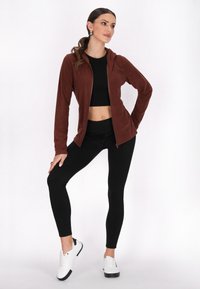 Hanorac crem cu fermoar, dotat cu glugă, purtat alături de un top negru scurt și colanți negri. Modelul poartă adidași albi cu accente negre.