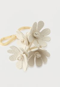 Biały skórzany brelok w kształcie kwiatu z trzema płatkami i metalowym klipsem w kolorze złotym. Posiada teksturowane płatki oraz gładkie centrum kwiatu.