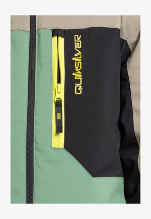 Hybrid-Jacke mit grünen, schwarzen und beige Panels, ausgestattet mit einem auffälligen gelben Reißverschluss und dem "Quiksilver"-Logo in leuchtendem Gelb auf der Vorderseite.