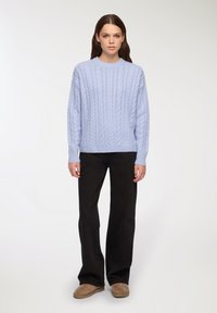 Jasnoniebieski sweter w splot kablowy z okrągłym dekoltem, długimi rękawami, zestawiony z czarnymi dzwonami i beżowymi butami wsuwanymi.