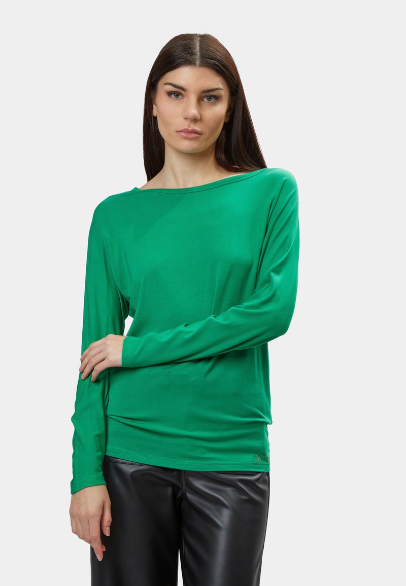 Grünes Langarmshirt aus weichem, dehnbarem Material mit weitem Ausschnitt, kombiniert mit schwarzen, figurbetonten Hosen. Verfügt über eine glatte Textur.