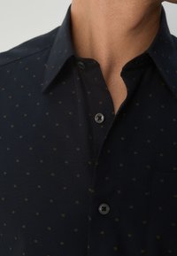 Marineblaues Hemd mit Knöpfen, das ein kleines quadratisches Muster in Gold zeigt, einen klassischen Kragen, eine aufgesetzte Tasche und eine glatte, leichte Stoffoberfläche aufweist.