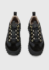 Scarpe da ginnastica nere realizzate in mesh e suede, con occhielli dorati, cuciture bianche a contrasto, suola testurizzata e un passante.