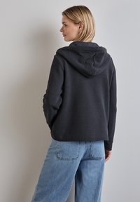Felpa con cappuccio grigio scuro, dalla superficie tinta e texturizzata, design aderente e tasca a marsupio, abbinata a jeans a gamba larga blu chiara.