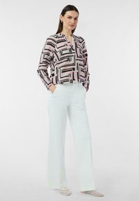 Bluzka z długim rękawem w geometryczny różowo-czarny wzór, z dekoltem w serek i luźnym kroju; zestawiona z białymi spodniami o szerokich nogawkach.