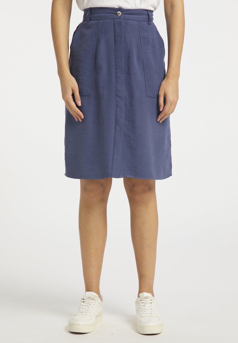 Blauwe knie-lange rok met een knoopsluiting, voorzien van twee voorzakken en een gladde textuur. Gecombineerd met witte sneakers voor een contrast.
