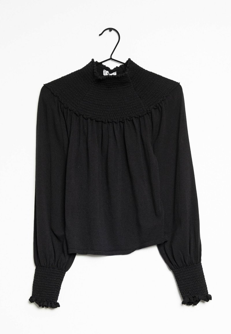 Blouse noire à manches longues avec col et poignets smockés hauts, suspendue à un cintre noir sur un fond blanc.