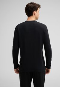 Schwarz langarm Shirt aus strukturiertem Stoff, mit Rundhalsausschnitt und lockerer Passform, seitlichen Schlitzen und einem kleinen Markenetikett am Saum.