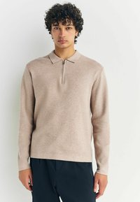 Långärmad, ljusbeige polo med kvart dragkedja och en strukturerad tyg. Enfärgad design, krage och rak nederkant.