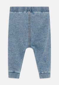 Pantalons en denim pour bébé en bleu clair, avec une taille et des poignets côtelés, présentant des coutures visibles le long des coutures et un design fuselé.