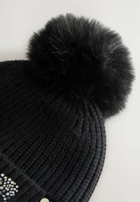 Black knitted beanie with a large black faux fur pom-pom on top. Features a row of sparkling rhinestones near the brim.