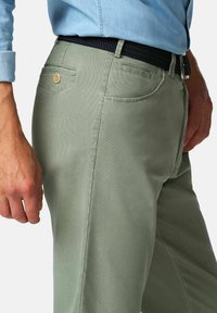 Groene broek van textuurstof, met een achterzak met een knoop en een geweven zwarte riem. Zijaanzicht getoond.