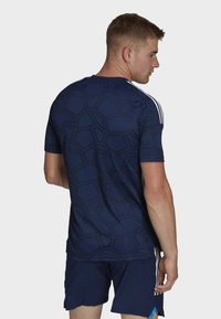 Marinefarbene Sportshirt mit geometrischem Muster, kurzen Ärmeln und drei weißen Streifen an den Schultern. Getragen mit passenden Shorts.