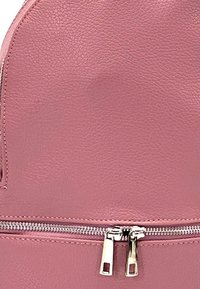 Sac à dos en cuir rose avec une texture, équipé d'une fermeture éclair argentée et de tirettes de fermeture éclair doubles à l'avant. Design simple et arrondi.