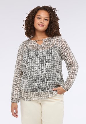 Durchsichtige Bluse mit langen Ärmeln in Schwarz und Creme mit einem Karomuster, ausgestattet mit einem Schlüsselloch-Ausschnitt und einem elastischen Saum, kombiniert mit hellen Hosen.