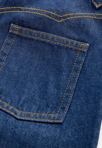 Gros plan sur un tissu en denim bleu montrant une poche arrière avec des coutures orange sur un jean.