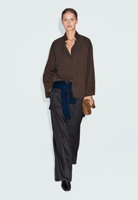 Bruine button-up shirt, donkerblauwe gewikkelde riem, grijs streepjespatroon wijde broek, bruine clutch en zwarte haklaarzen. Gladstof texturen.