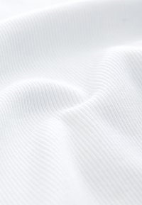 Gros plan d’un tissu blanc côtelé avec des plis doux et une texture lisse.
