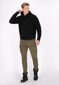 Sort bomulds hoodie med frontlomme, parret med olivengrønne cargo-bukser med sidelommer og sorte læderstøvler.