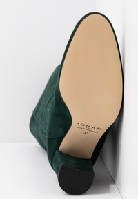 Botte cheville en daim vert, vue en angle montrant la semelle beige lisse avec la marque, la taille 37, et l'inscription "Fabriqué au Portugal".