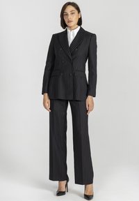 Czarny garnitur w paski z podwójnym zapięciem i szerokimi spodniami. Posiada ostrą kołnierz i kieszenie. Błyszczące czarne szpilki.
