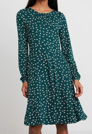 Sukienka z długim rękawem w kolorze teal, wykonana z lekkiego materiału, ozdobiona białym kwiatowym wzorem. Marszczony dekolt oraz rozkloszowany dół.