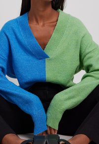 Suéter ligero de punto con cuello en V, con un diseño dividido en tonos azules y verdes. Puños acanalados y textura de ajuste relajado.