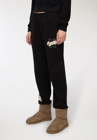 Czarne spodnie dresowe z elastycznym pasem i białym logo "Brooklyn N". Połączone z brązowymi zamszowymi botkami do kostki z płaską podeszwą.