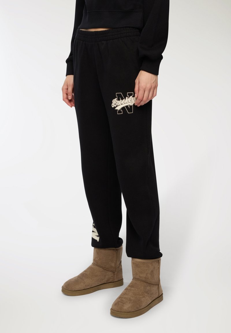 Czarne spodnie dresowe z elastycznym pasem i białym logo "Brooklyn N". Połączone z brązowymi zamszowymi botkami do kostki z płaską podeszwą.