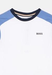 Κοντομάνικο T-shirt με λευκό σώμα, μανίκια raglan σε μπλε και ναυτικό χρώμα, στρογγυλή λαιμόκοψη και λογότυπο «BOSS» στο στήθος. Κατασκευασμένο από βαμβάκι.