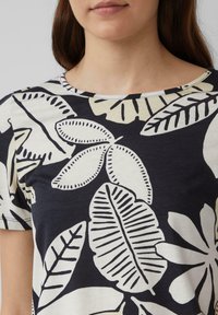 T-shirt à manches courtes, noir et crème, présentant de grands motifs de feuilles audacieux. Matière en coton avec un col arrondi et une coupe décontractée.