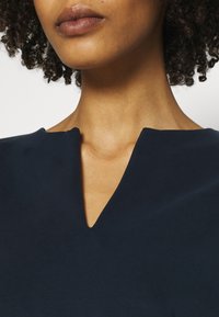 Mörkblå, mjuk tygöverdel med V-formad nøckline. Minimalistisk design med slät textur och rena kanter runt kragen.