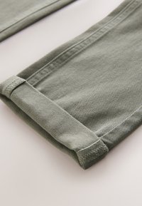 Close-up of light green denim pant legs with cuffs folded up on a light background.