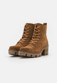 Botas de tobillo de ante marrón con puntera redonda, diseño de cordones, suela de goma contrastante y un tacón grueso con ranuras horizontales.