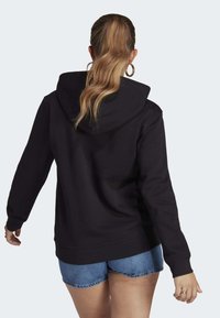 Schwarzer Hoodie mit großer Kapuze, langen Ärmeln und gerippten Bündchen. Kombiniert mit Jeansshorts, zeigt ein lässiges Design und eine weiche Textur.
