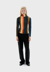 Long-sleeve, turtleneck top in striped pattern featuring shades of blue, orange, brown, and cream; paired with black trousers and shoes.