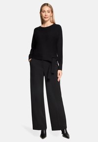 Czarny sweter dzianinowy z długimi rękawami, z wiązanym akcentem w talii. Połączony z szerokimi czarnymi spodniami i spiczastymi czarnymi botkami.